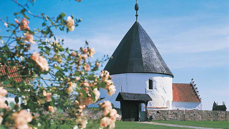 Rundkyrka på Bornholm med vitkalkade murar och koniskt tak, ett historiskt landmärke från medeltiden i naturskön dansk miljö.