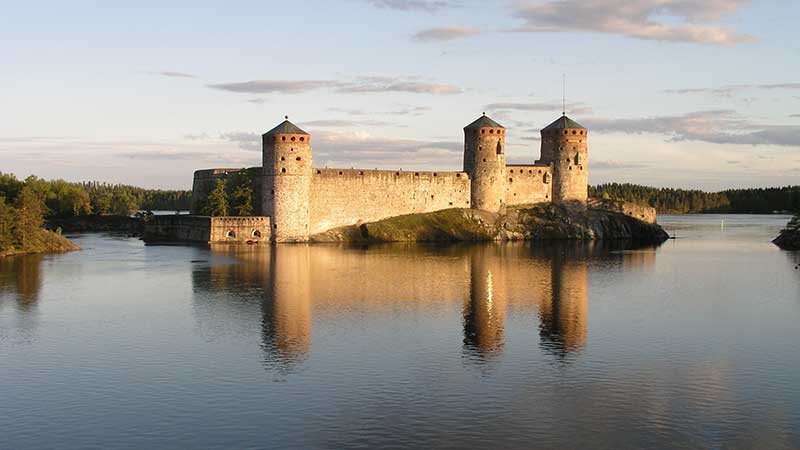 Savonlinna i solnedg�ng � silhuetten av Olavinlinna slott och stadens �ar speglas i sj�n Saimaa