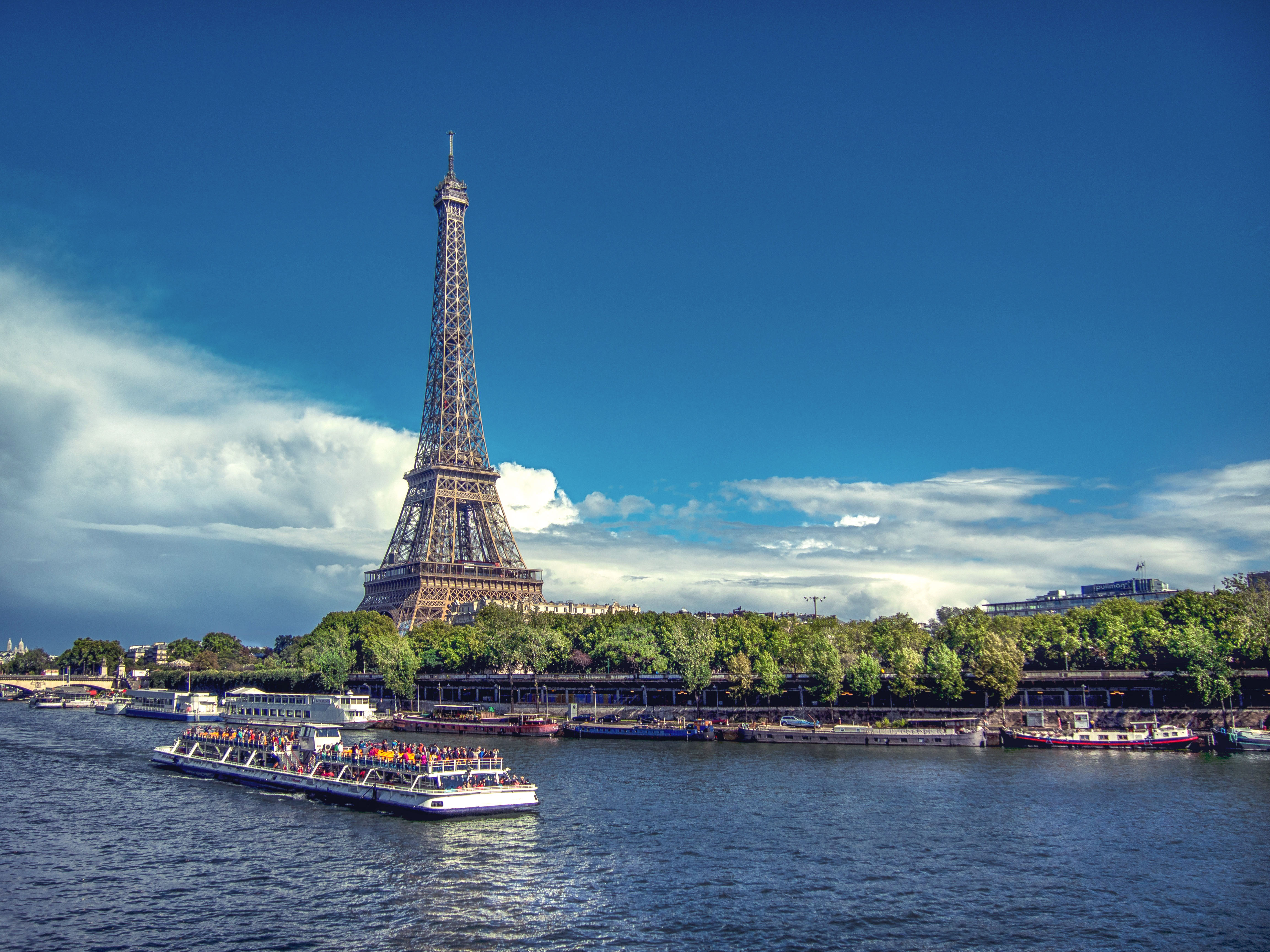 Eiffeltornet i Paris sett fr�n floden Seine med sightseeingb�t i f�rgrunden under klarbl� himmel.