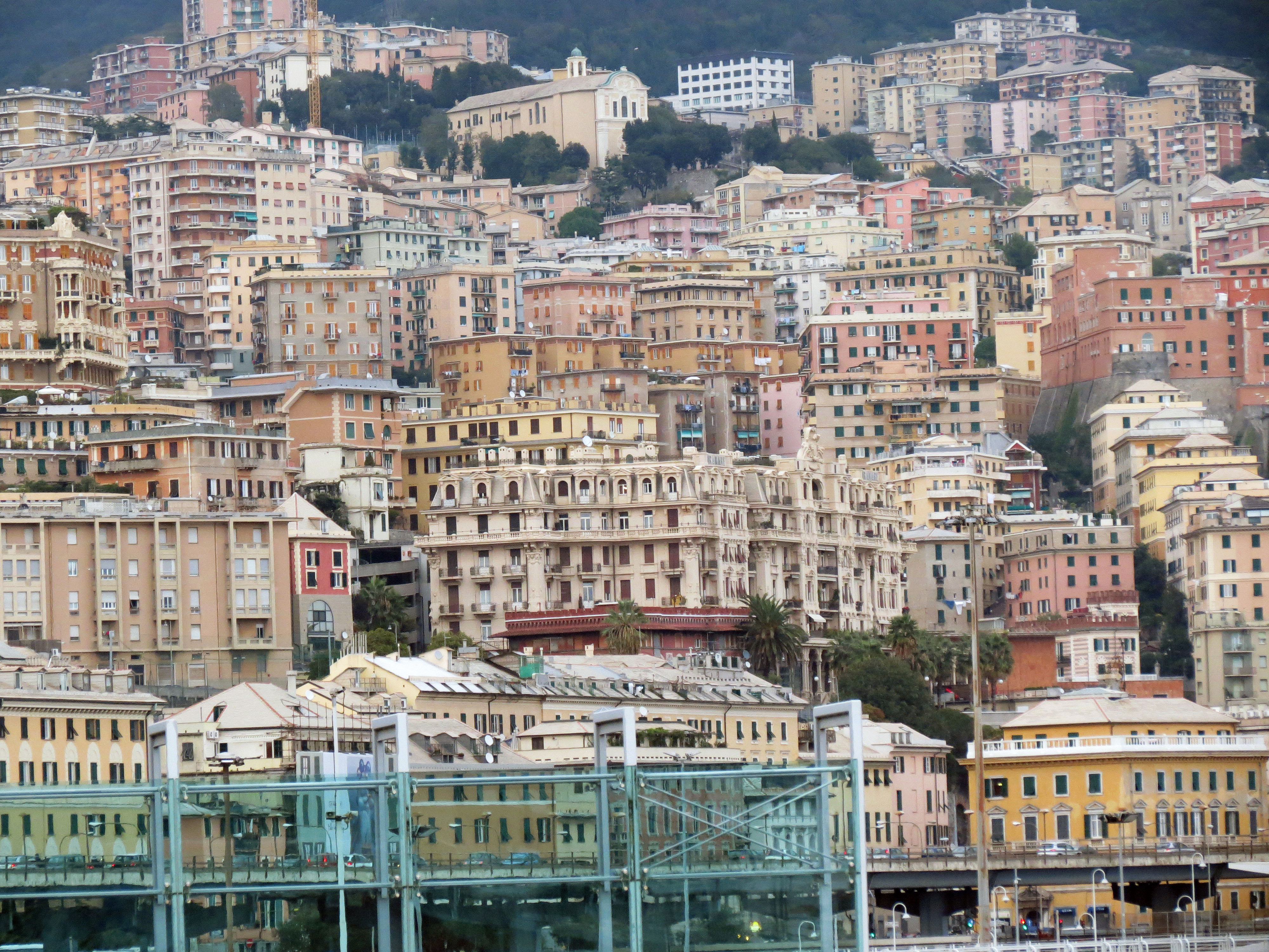 Panoramavy �ver t�tbebyggda historiska och moderna byggnader i Genua, Italien, med kuperad bakgrund och arkitektonisk m�ngfald.