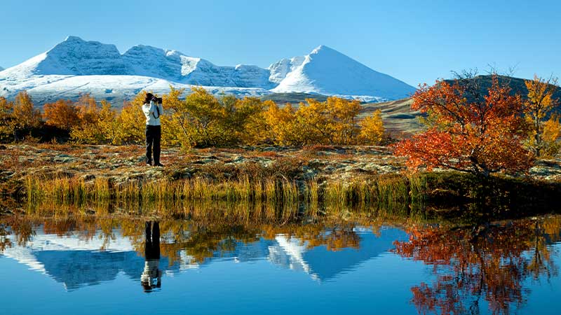 Rondane i h�stf�rger � klart vatten speglar sn�t�ckta fj�ll och gyllene dalg�ngar i norsk natur. Upplev det med Tj�rnarpsbuss bussresa