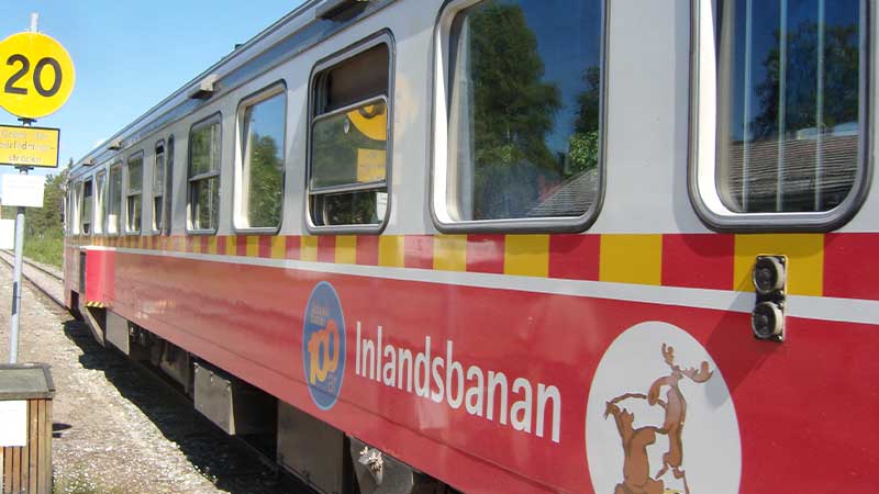 N�rbild p� Inlandsbanans r�da t�g � klassisk svensk r�lsbuss mot norr genom skogar och vildmark. F�lj med Tj�rnarpsbuss p� en tur
