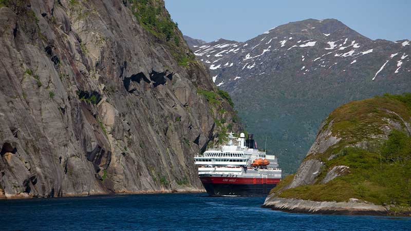 Hurtigruten glider fram på vatten mellan norska fjäll – en majestätisk resa genom berg och kust. En del av Tjörnarpsbuss resa till Norge