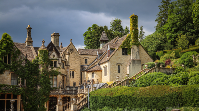 Charmigt stenhus i Cotswolds, England, omgivet av grönskande trädgård och klätterväxter – typisk engelsk landsbygdsmiljö.