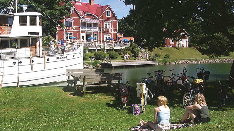 Göta Hotell vid Göta kanal med båtar och vatten – klassisk svensk sommarupplevelse. Upplev det med Tjörnarpsbuss