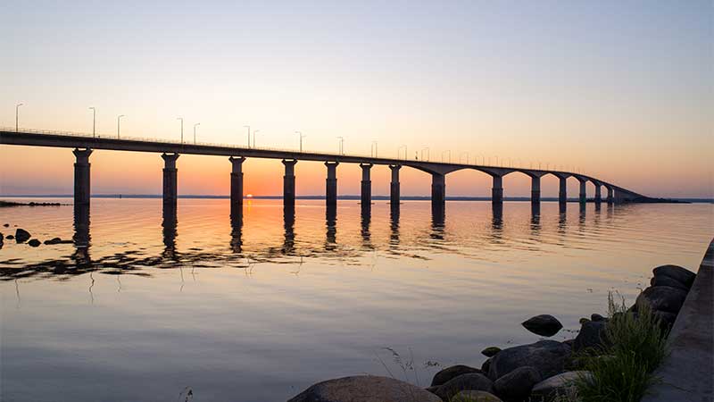 Ölandsbron vid solnedgång med mjukt ljus som speglas i det stilla vattnet, lång broförbindelse mellan Kalmar och Öland i Sverige.